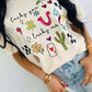 Person wearing a white t-shirt with colorful lucky you lucky me western cowboy graphics and text.
