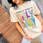 Woman wearing a Born to Dilly Dally Ivory  t-shirt with colorful text outdoors