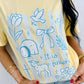 Person wearing a yellow t-shirt with blue illustrations and IT IS FINISHED text.