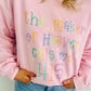 Person wearing a pink sweatshirt with colorful text design, the maker of heaven calls me HIS, standing against a plain background.