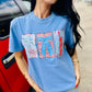 Woman wearing a blue t-shirt with graphic designs, standing next to a red car.