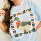 Woman wearing a light blue t-shirt with a duck mallard patchwork graphic design.