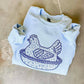 White sweatshirt with blue graphic design on a beige surface