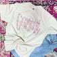 White t-shirt with colorful 'Gammi' text on a multicolored patterned surface