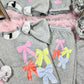 Gray sweatshirt and pants set with colorful bows on a pink surface.