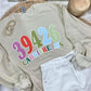 Beige sweatshirt with colorful zipcode  text on a bed