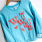 Light blue sweatshirt with coral puff text WWJD and cross, bow, heart leaf graphics on a white tiled floor