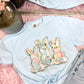 Light blue t-shirt with water color brushed floral bunny design on a pink surface