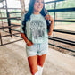 A person standing in an outdoor setting wearing a blue t-shirt with 'Rolling Stones' text and a graphic of a stone on it, paired with denim shorts.