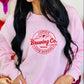 Person wearing a pink sweatshirt with 'Cupid's Brewing Co' print, surrounded by heart-shaped objects.