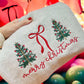 White sweatshirt folded with Christmas tree and bow design held by a hand against a colorful background of balloons.