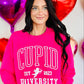A person wearing a pink sweatshirt with the text 'CUPID UNSUCCESSFUL SINCE 1823' and a graphic of a cupid, surrounded by heart-shaped balloons.