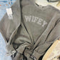 A gray sweatshirt with the word 'WIFEY' embroidered in white on the front, displayed on a rack with other clothing items.