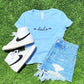 Light blue t-shirt with 'devils' text, white high-top sneakers, and denim shorts on grass