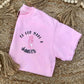 Pink t-shirt with 'So God Made a Dancer' text on a woven mat with beads and tassels.