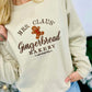 A woman wearing a beige embroidered sweatshirt with 'MRS. CLAUS' GINGERBREAD BAKERY' text and a cute gingerbread man graphic.