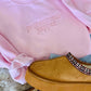 A light pink embroidered sweatshirt with the text 'PROFESSIONAL YAPPER' on the front, placed on a white furry surface, with a pair of blue jeans and a pair of tan casual shoes with embellished sole patterns on a matching white furry surface.
