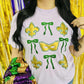 A person wearing a purple t-shirt with a green and gold bow design with masks and the text 'Mardi Gras' on it, standing in a glittery background.