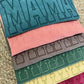Stack of colorful fabric samples with 'MAMA' text on a textured surface