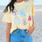 A person wearing a yellow graphic tee with seafood-themed designs and blue denim shorts, standing on a beach.