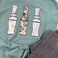 Green t-shirt with three camouflaged duck call designs on a white surface.