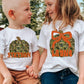 Two children wearing white t-shirts with custom pumpkin designs with names, sitting on a hay bale outdoors.