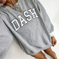 Person wearing a gray sweatshirt with 'DASH' printed on it, sitting on a white surface.