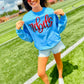 Woman wearing a blue sweatshirt with 'Rebels' on it, standing on a grassy field.