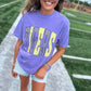 Woman wearing a purple t-shirt with yellow text on a sports field
