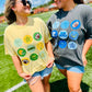 Two women standing on a grassy field wearing t-shirts with colorful circular patterns.