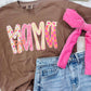 Brown t-shirt with 'MAMA' print, pink shorts, and denim shorts on a white surface.