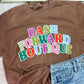Brown t-shirt with 'Dash Forward Boutique' text and blue jeans on a light pink surface