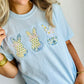 Woman wearing a light blue t-shirt with embroidered designs of Easter bunny bow patchwork and flowers.