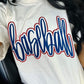 White t-shirt with 'baseball' printed in blue puff vinyl and red glitter on a person sitting in a car.