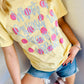 Person wearing a yellow t-shirt with text "What a friend we have in Jesus" polka dots and pink hearts, sitting against a light-colored wall.