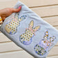 Hand holding a folded embroidered tee with lace bunny designs against a wooden background