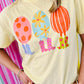 Person wearing a yellow t-shirt with colorful egg and boots balloon designs on a multicolored striped background
