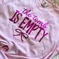 Pink t-shirt with 'the tomb is empty' text in purple on a textured surface