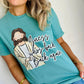 Person wearing a teal t-shirt with a Jesus "guess who is back again" graphic design and text.