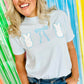 Person wearing a white t-shirt with blue designs with Puff Peeps Bunny and glitter bows against a colorful striped background