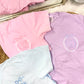Pastel-colored shirts with embroidered designs on a textured surface.