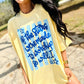 Person wearing a yellow t-shirt with blue text and star graphics outdoors.