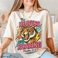 Person wearing a t-shirt with a graphic design of a tiger and text "Heavens are roaring", sitting on a couch.