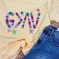 Yellow t-shirt with colorful 'G>^V' text and denim shorts on a textured surface