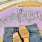 Pair of beaded sandals on jeans with a purple pillow and decorative text in the background