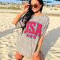 Woman wearing a bottomland 'USA' t-shirt on a sandy beach.