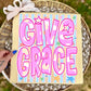 Decorative sign with 'Give Grace' text on a striped background, held over a woven basket.