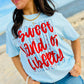 Woman wearing a light blue t-shirt with 'Sweet Land of Liberty' text on a beach.
