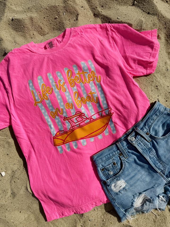 Pink t-shirt with 'Life is better on a boat' graphic and denim shorts on sand