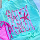 Mint green tank top with pink starfish design and text, paired with a pink bikini bottom on a concrete surface.